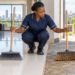 A Black African cleaner compares a soft indoor broom with a stiff outdoor broom.