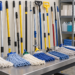 A Black African cleaner compares sturdy mop handles in a facility supply room.