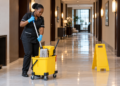 A Black African cleaner demonstrates a mop bucket and wringer on a tiled floor.