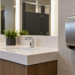 A Black African visitor uses a wall-mounted hand dryer in a clean washroom.